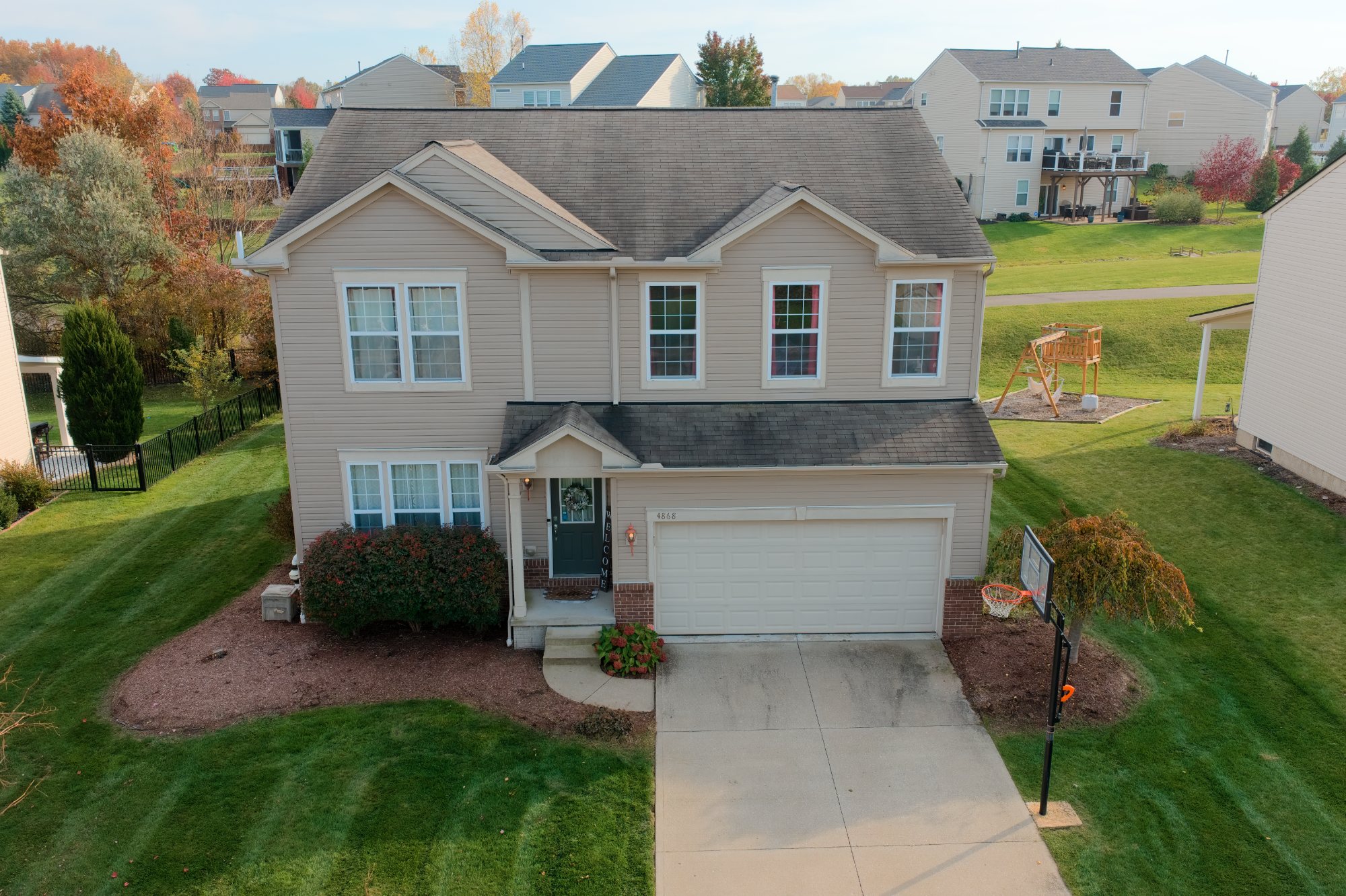Front of a two-story house with a two-car garage, landscaped beds and fall color behind