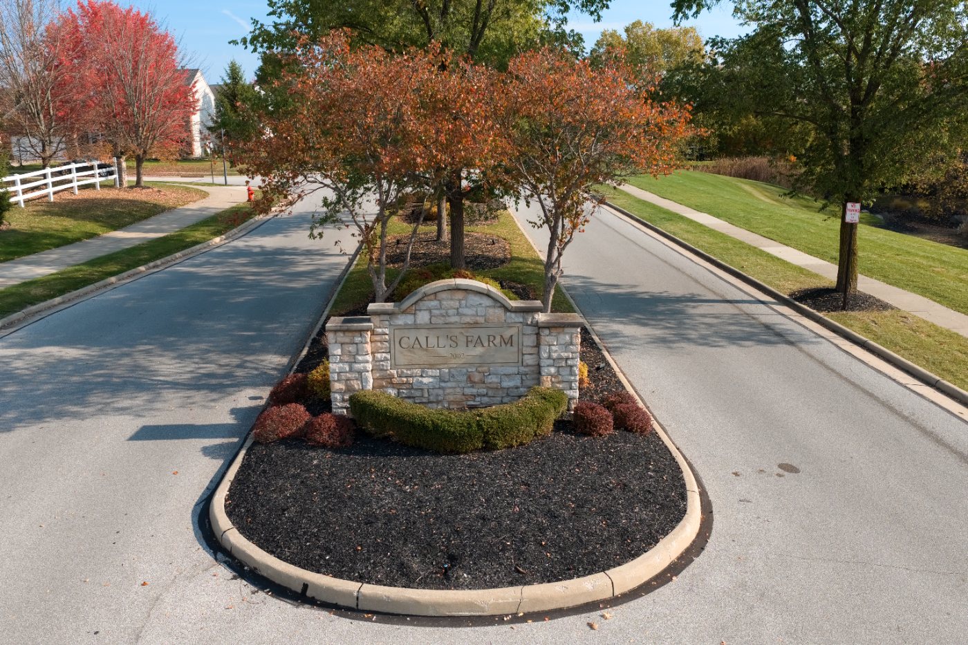 The neighborhood entrance sign on a landscaped median, framed by fall trees