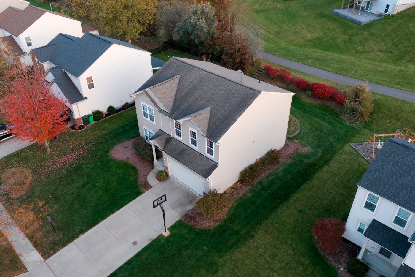 High view looking down on the front of the house, driveway and front lawn, with a play set and walking path behind