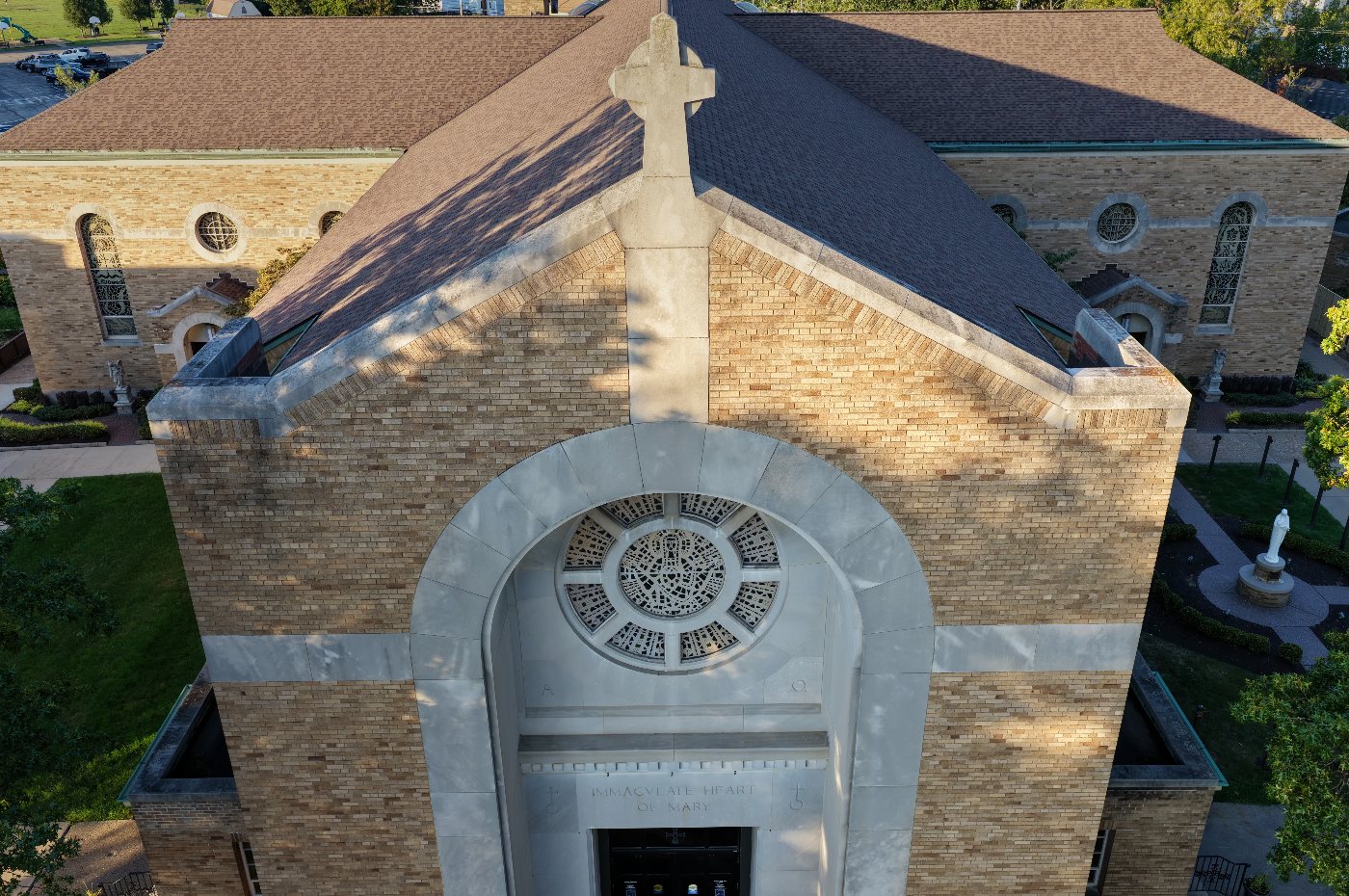 Aerial view of a brick church front with a stone cross, rose window and carved lettering in low sun