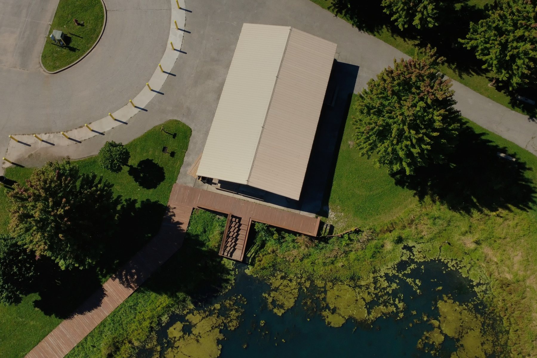 Straight-down view of a park pavilion roof, boardwalk and stairs down to a pond