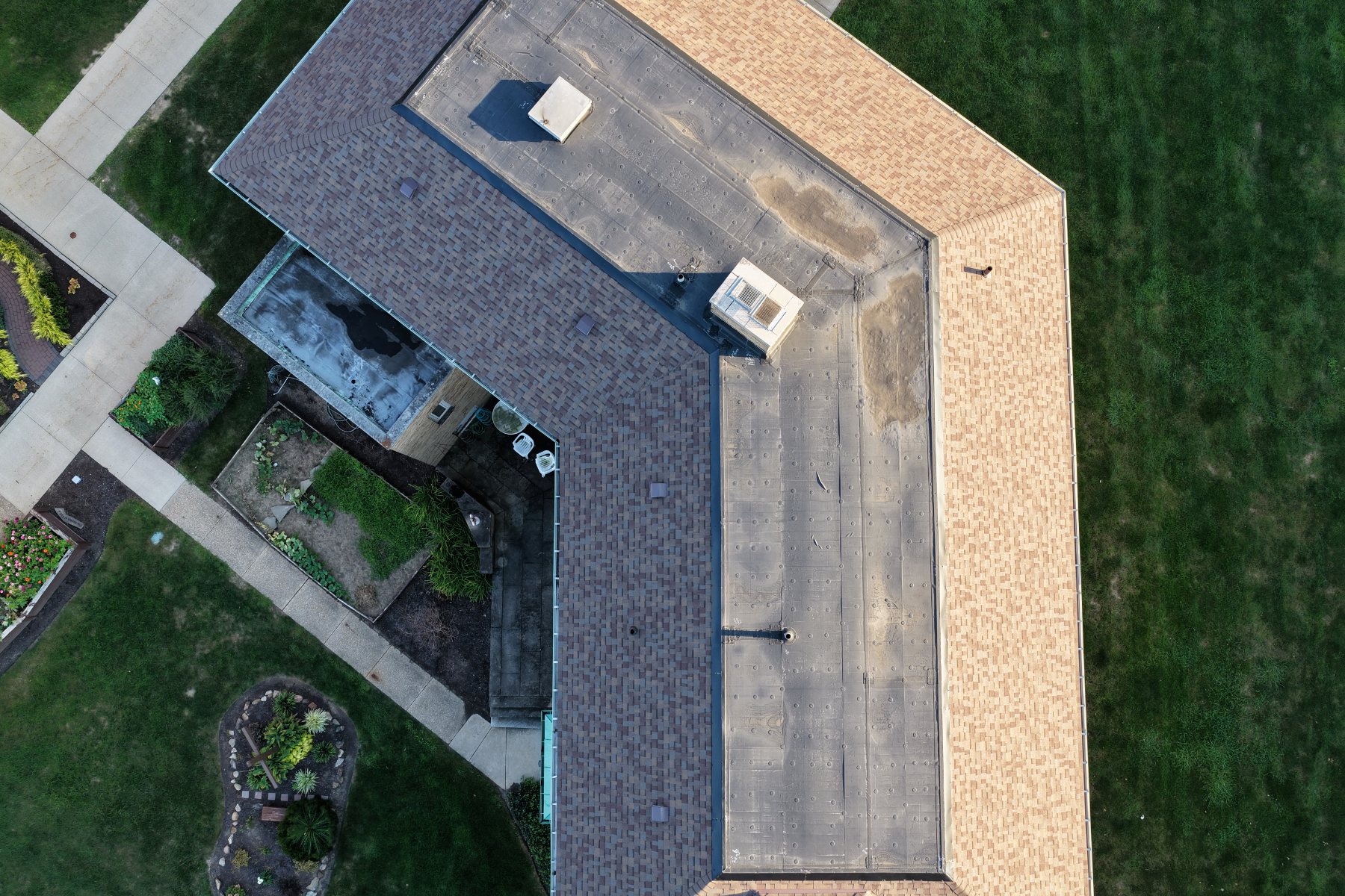 Straight-down view of a building roof showing shingle planes, flat sections, vents and gutter lines